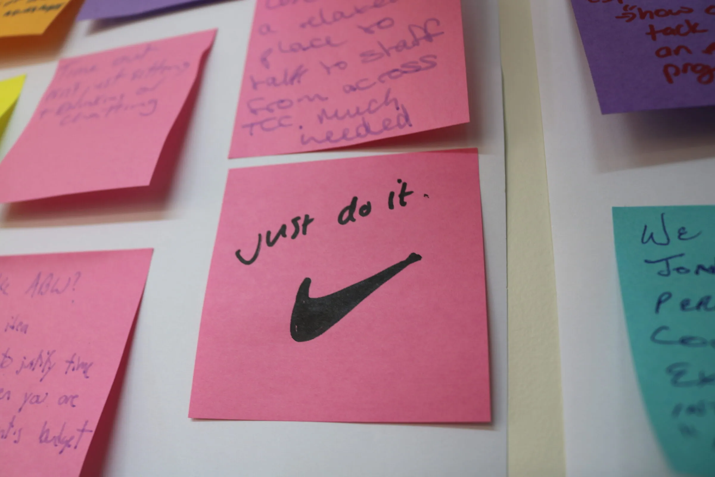 A pink sticky note on a workshop wall reading Just do it, among notes from a team session